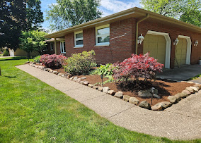 Stone-edged foundation bed with red shrubs along a brick ranch